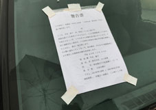放置車両のフロントガラスに警告書を貼付している様子